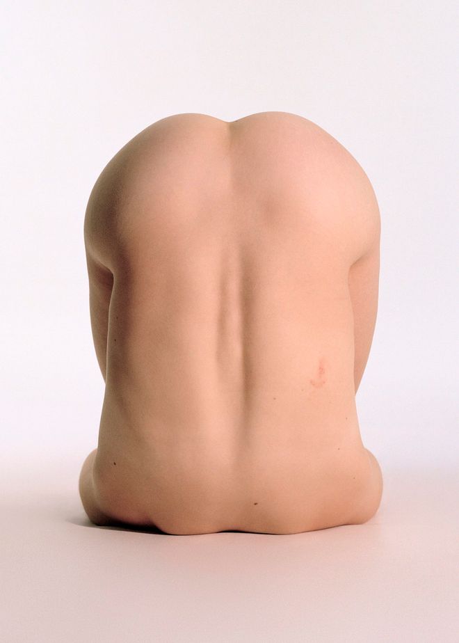 A colori, un corpo nudo raccolto su sé stesso visto di schiena.