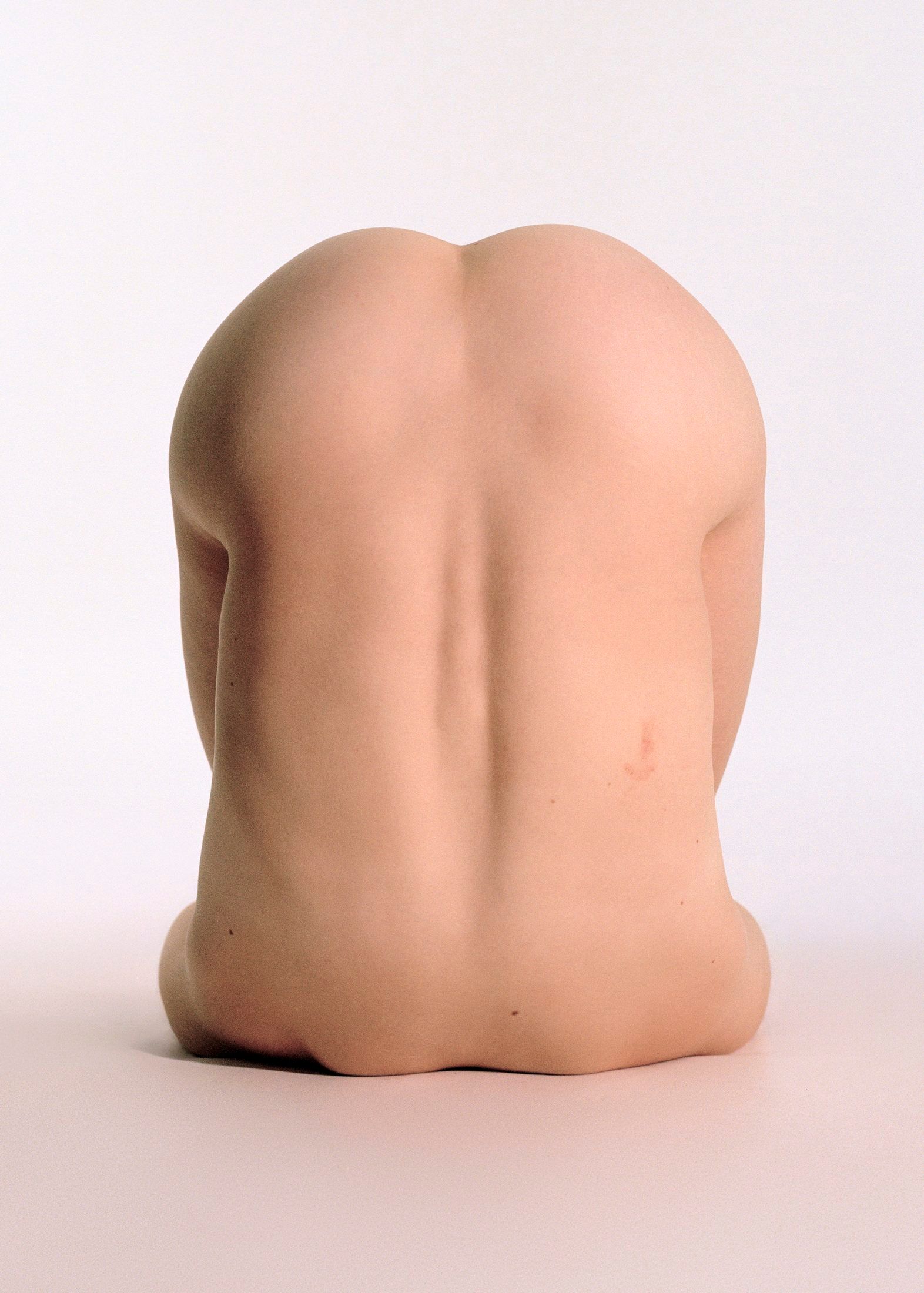 A colori, un corpo nudo raccolto su sé stesso visto di schiena.