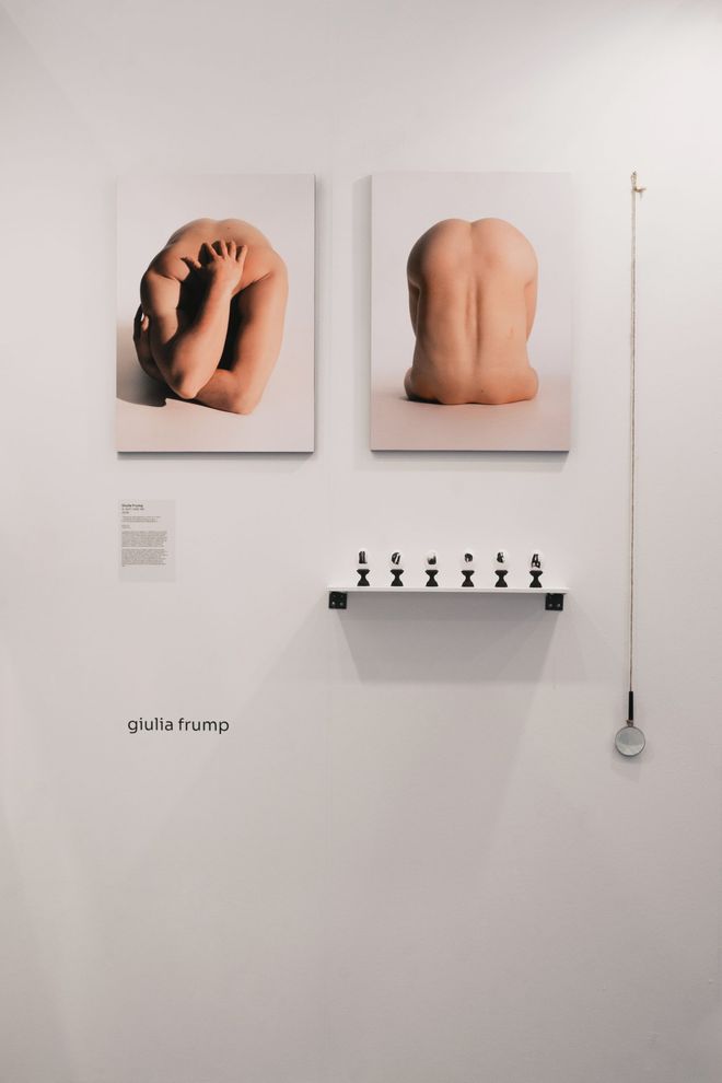 Allestimento in mostra: due fotografie del progetto, una mensola con sei uova su piedistalli e una lente appesa a un filo.