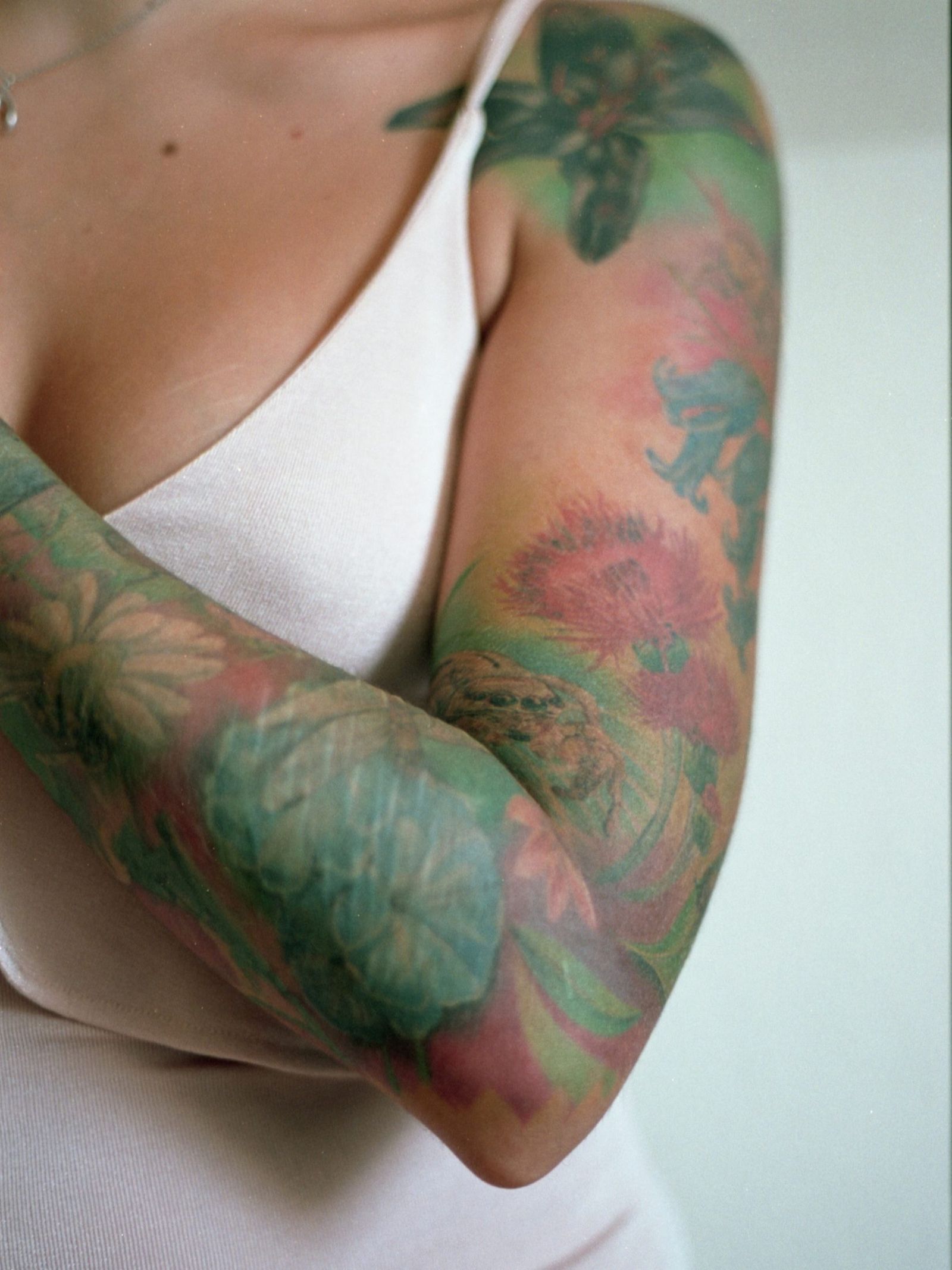Busto di una donna in canottiera bianca, con il braccio coperto da tatuaggi floreali tenuto davanti al corpo.