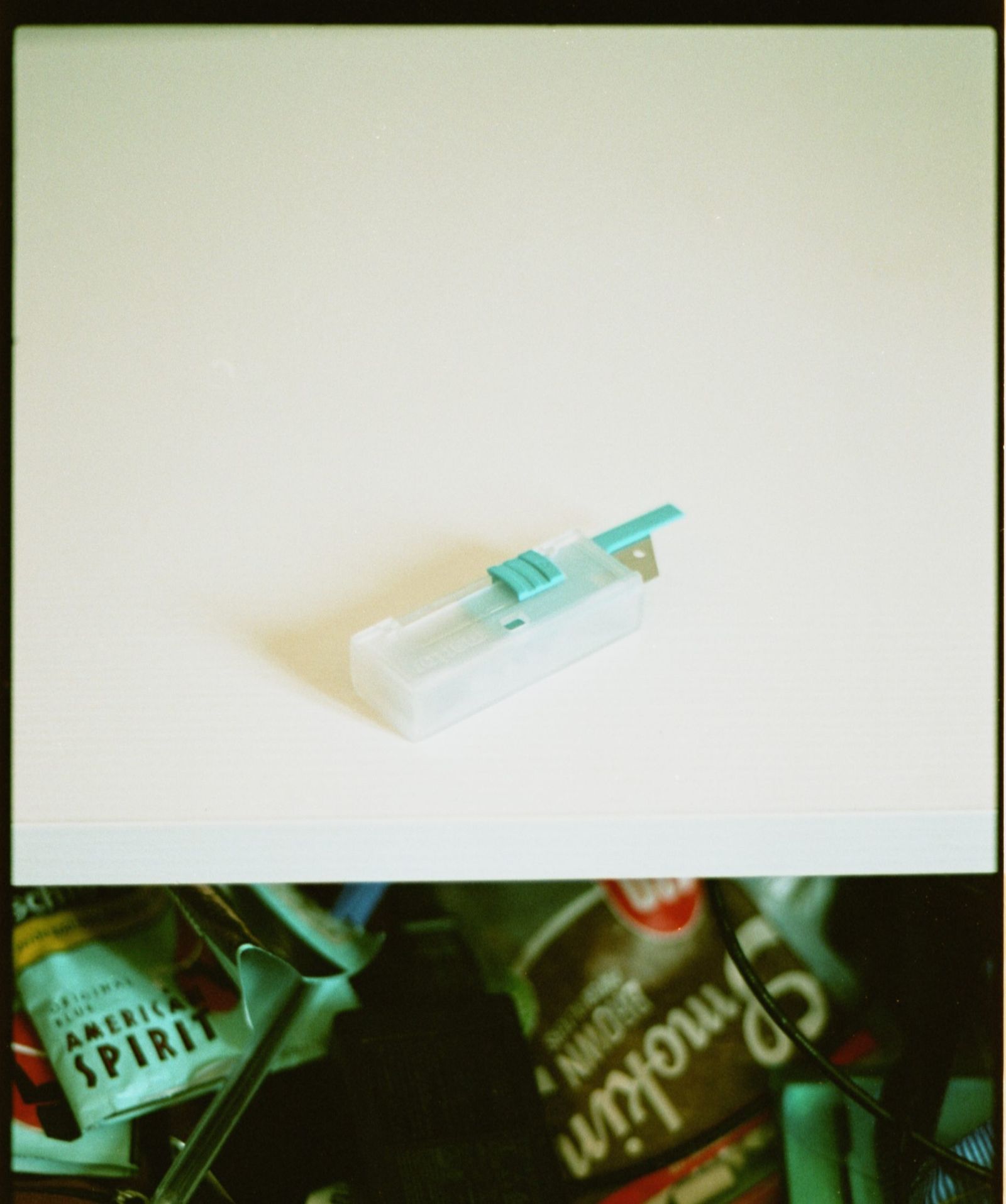 Una scatoletta di lamette su un piano bianco; sotto, un cassetto aperto con tabacco e cartine.