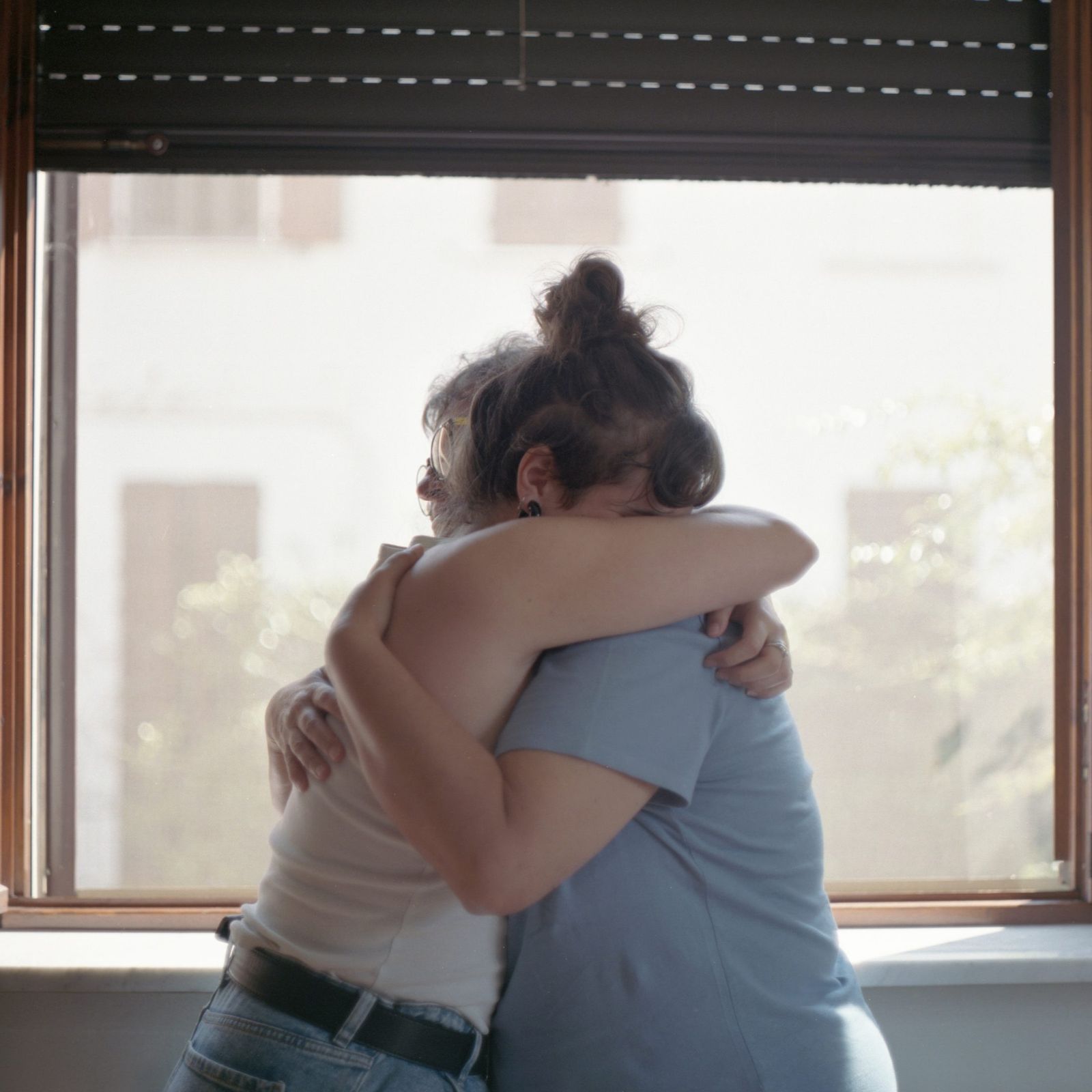 Due persone abbracciate davanti a una finestra luminosa.