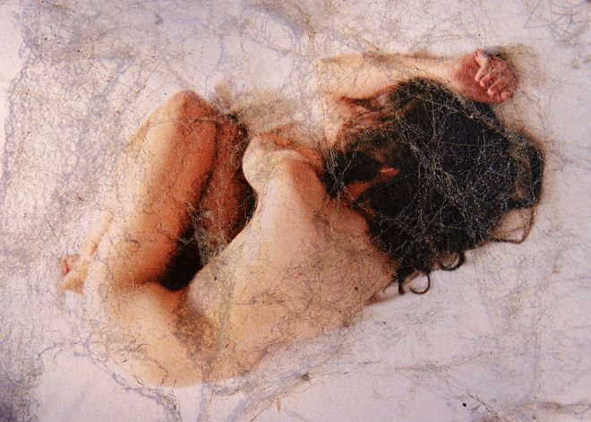 Una persona nuda rannicchiata, avvolta da una ragnatela.