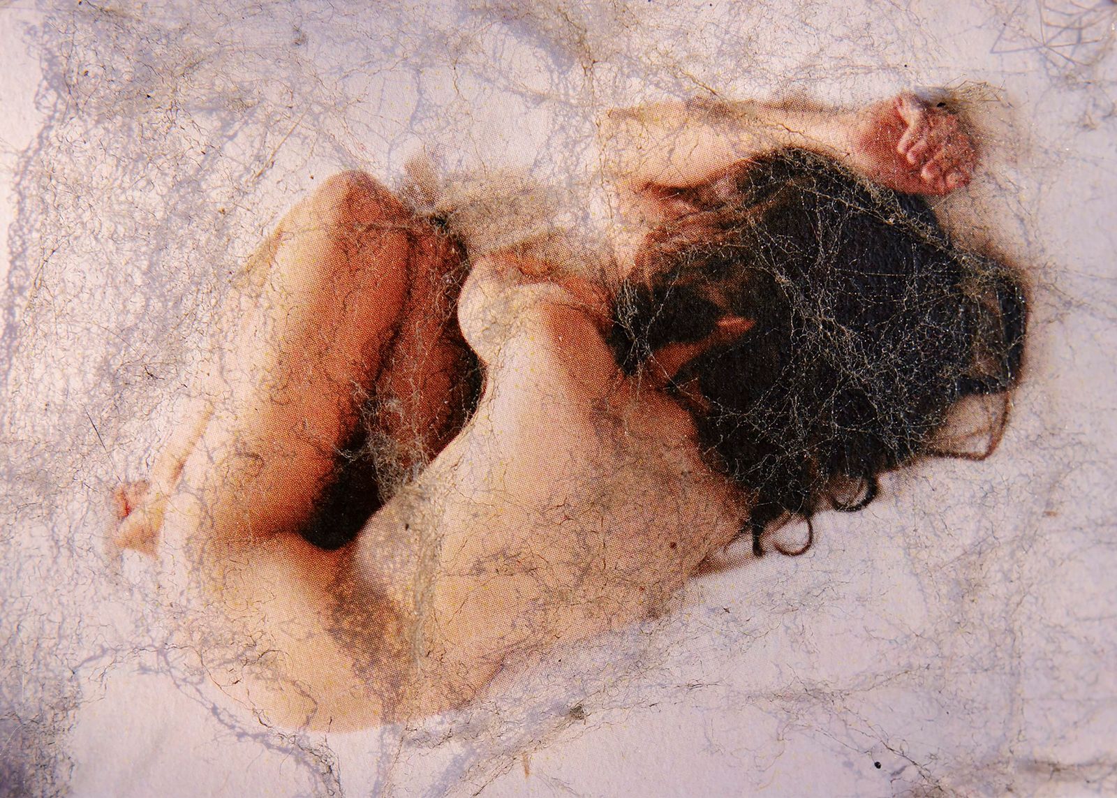 Una persona nuda rannicchiata, avvolta da una ragnatela.