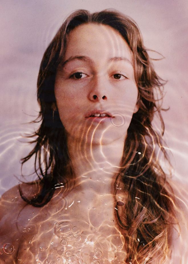Volto di una giovane donna che emerge dall'acqua, attraversato da riflessi di luce.