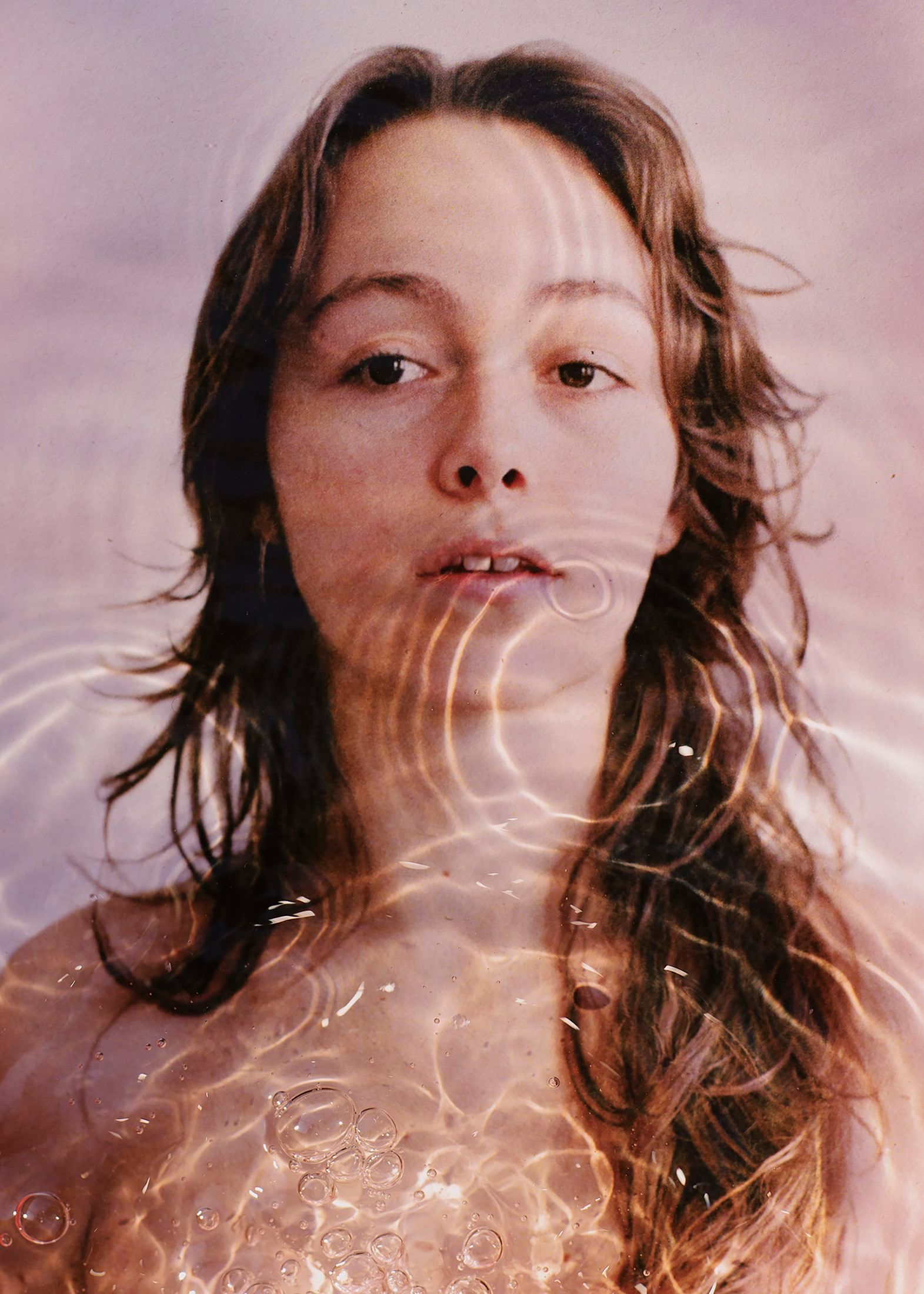 Volto di una giovane donna che emerge dall'acqua, attraversato da riflessi di luce.